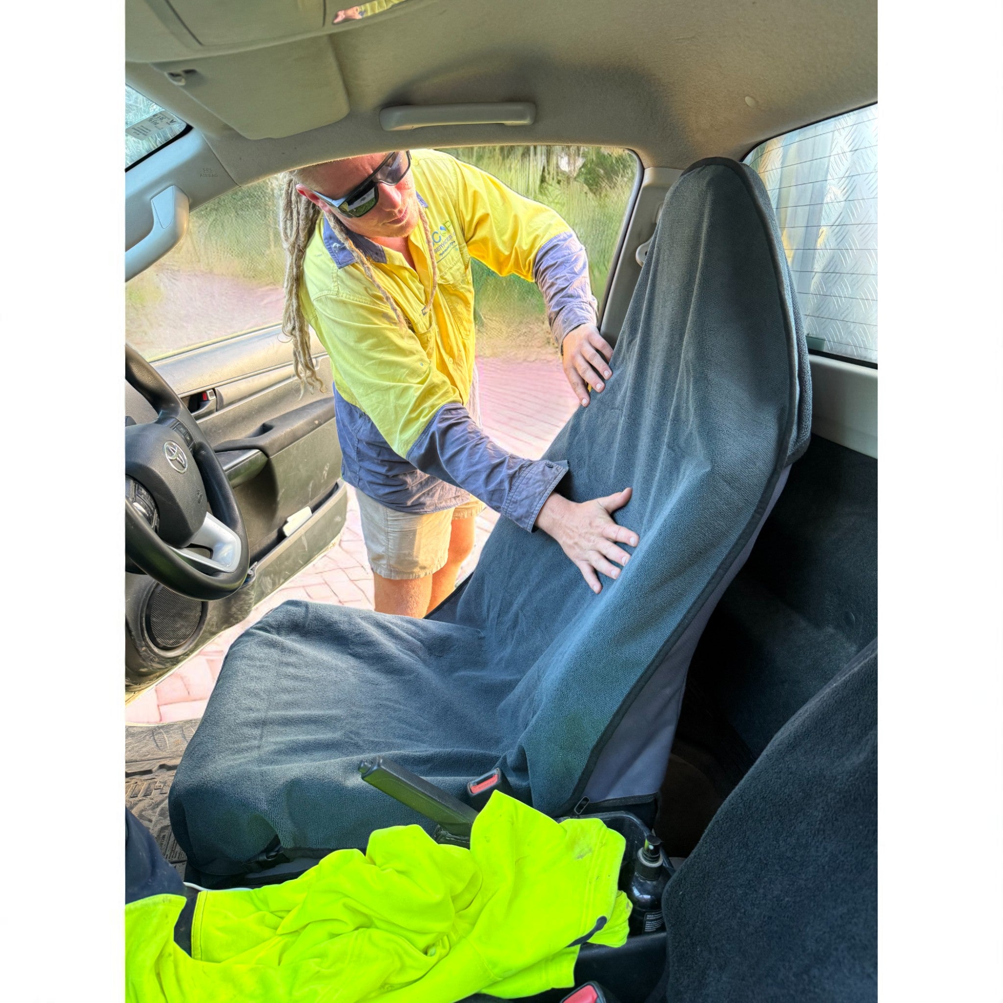 Tradesman in a hi-vis shirt putting on a navy blue waterproof car seat towel in his work ute.